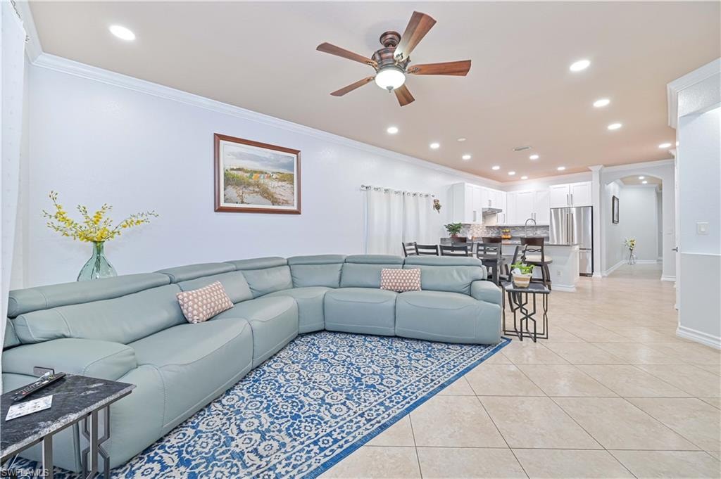 Living room featuring arched walkways, a ceiling fan, crown molding, light tile patterned floors, and recessed lighting