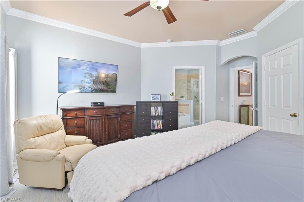 Bedroom with ornamental molding, arched walkways, ceiling fan, and ensuite bath