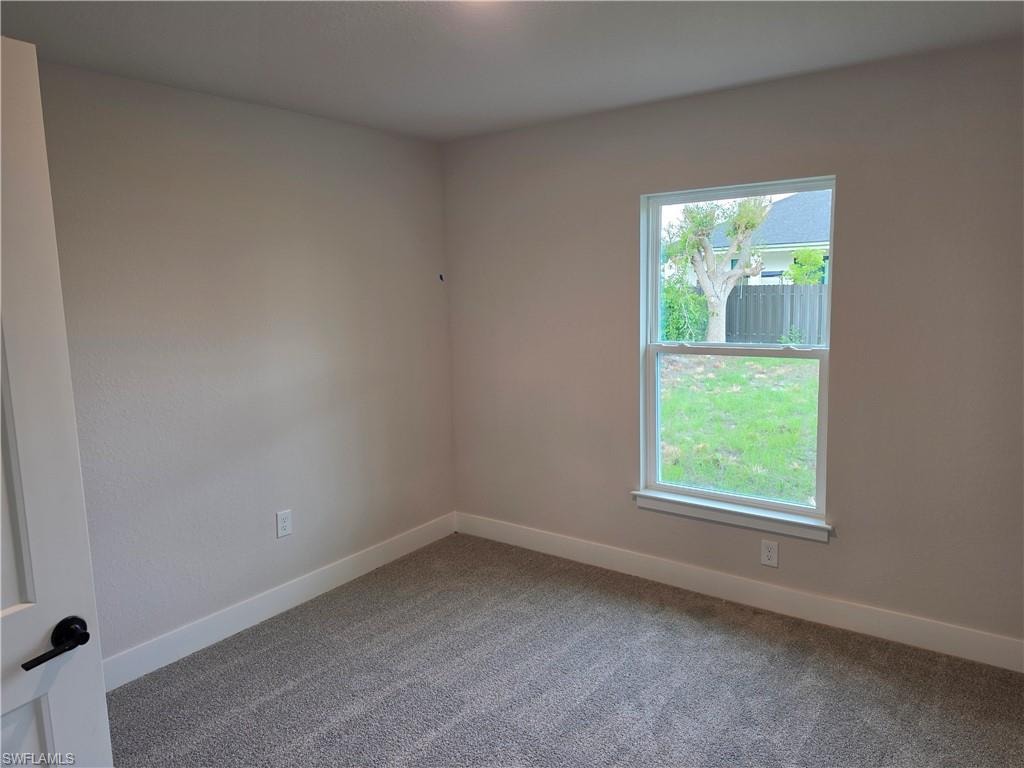 Light-filled room featuring neutral wall tones, plush gray carpeting, white trim, a double-hung window, and a modern interior door with matte black hardware