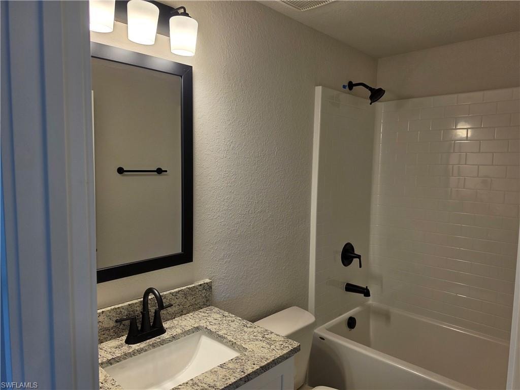 Bathroom featuring a granite-look vanity with an undermount sink and matte black faucet, a large framed mirror with tri-light fixture, and a subway-tile-patterned shower surround with matte black fixtures