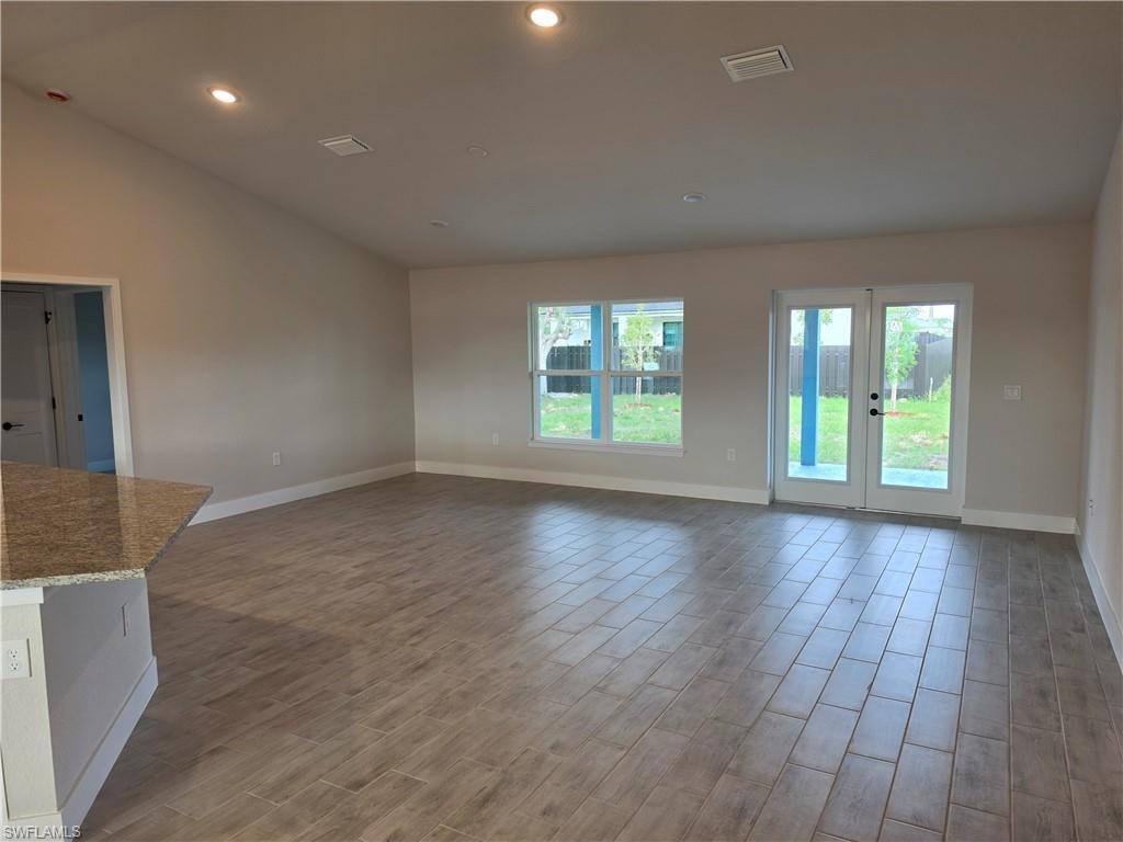 Spacious living area featuring plank-style tile flooring, vaulted ceilings with recessed lighting, and a kitchen island with a stone countertop