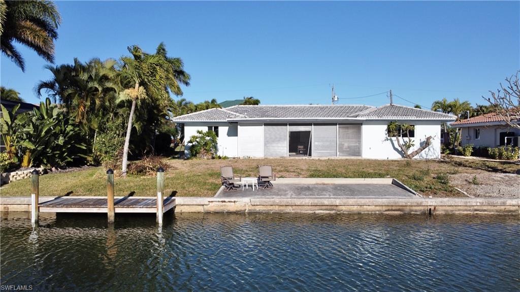 Rear view of house with a water view, a lawn, a patio, and a tile roof