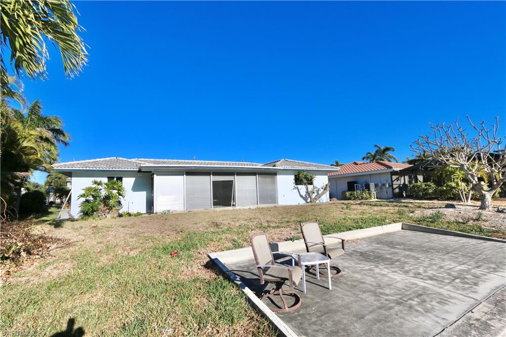 Rear view of property with a lawn, stucco siding, a tile roof, and a patio