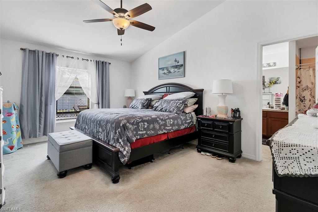 Bedroom with vaulted ceiling, light colored carpet, a ceiling fan, and ensuite bath