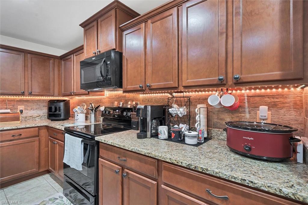 Kitchen with black appliances, light stone counters, and light tile patterned floors