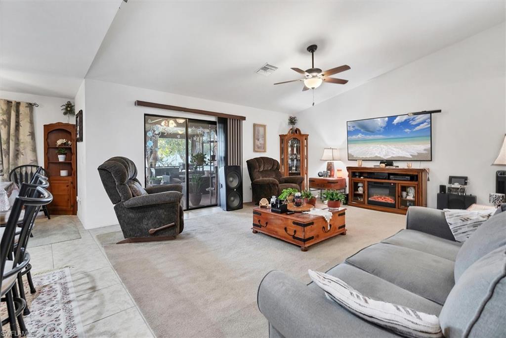Tiled living room featuring vaulted ceiling, a ceiling fan, and carpet