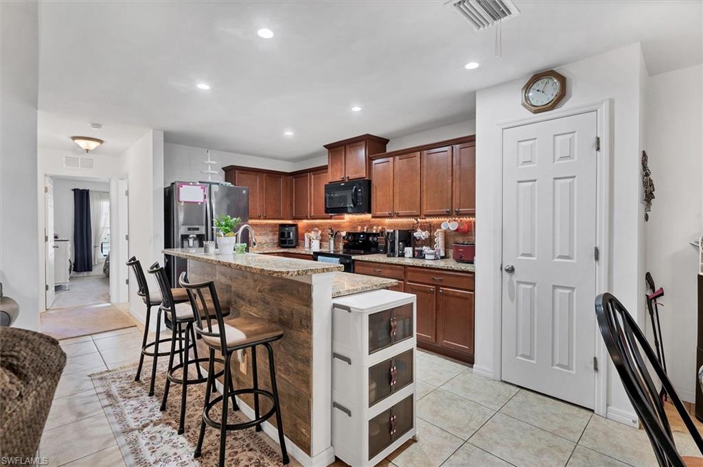 Kitchen with a kitchen island with sink, a kitchen breakfast bar, light stone counters, black appliances, and light tile patterned flooring