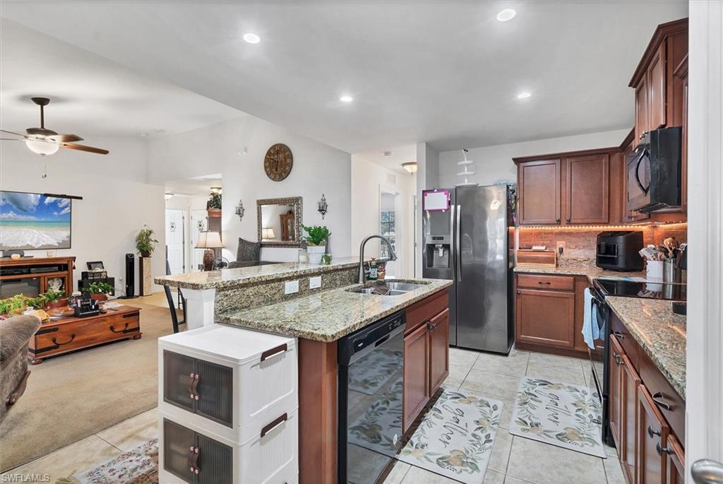 Kitchen featuring black appliances, light stone countertops, open floor plan, a center island with sink, and recessed lighting