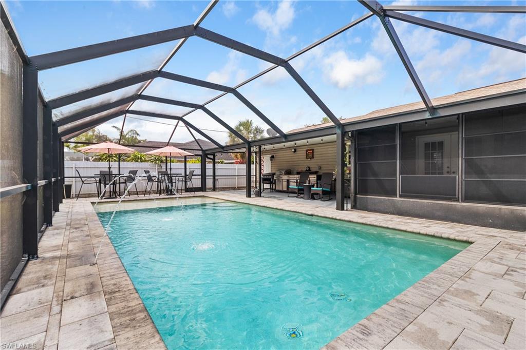 View of pool with a sunroom, glass enclosure, outdoor dining area, and patio surround