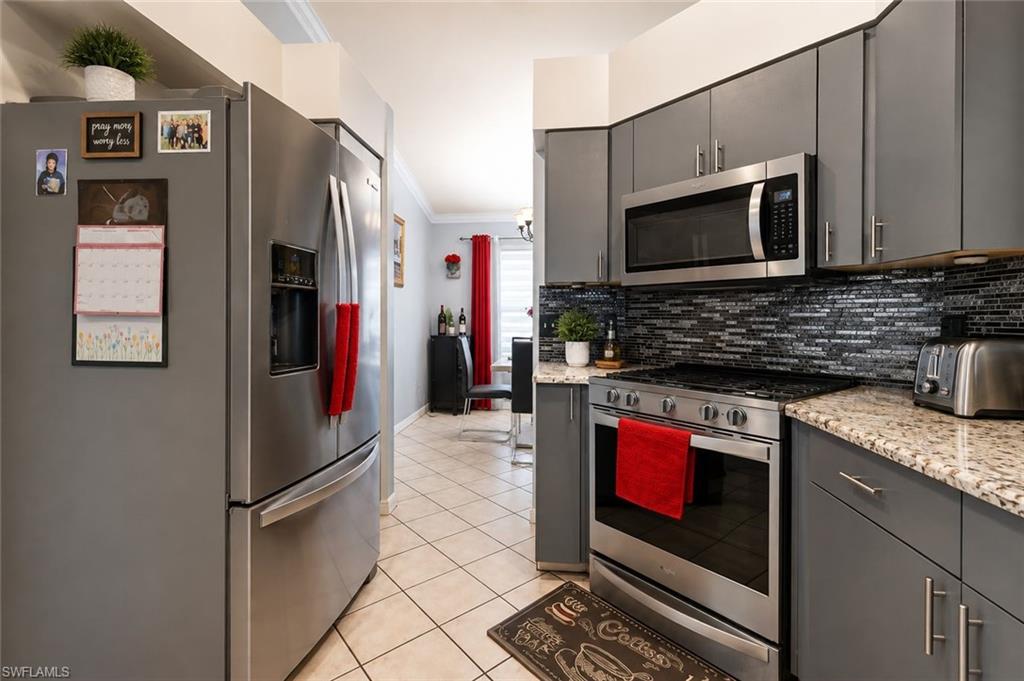 Two tone kitchen featuring stainless steel appliances, light stone counters, tasteful backsplash, crown molding, and light tile patterned flooring