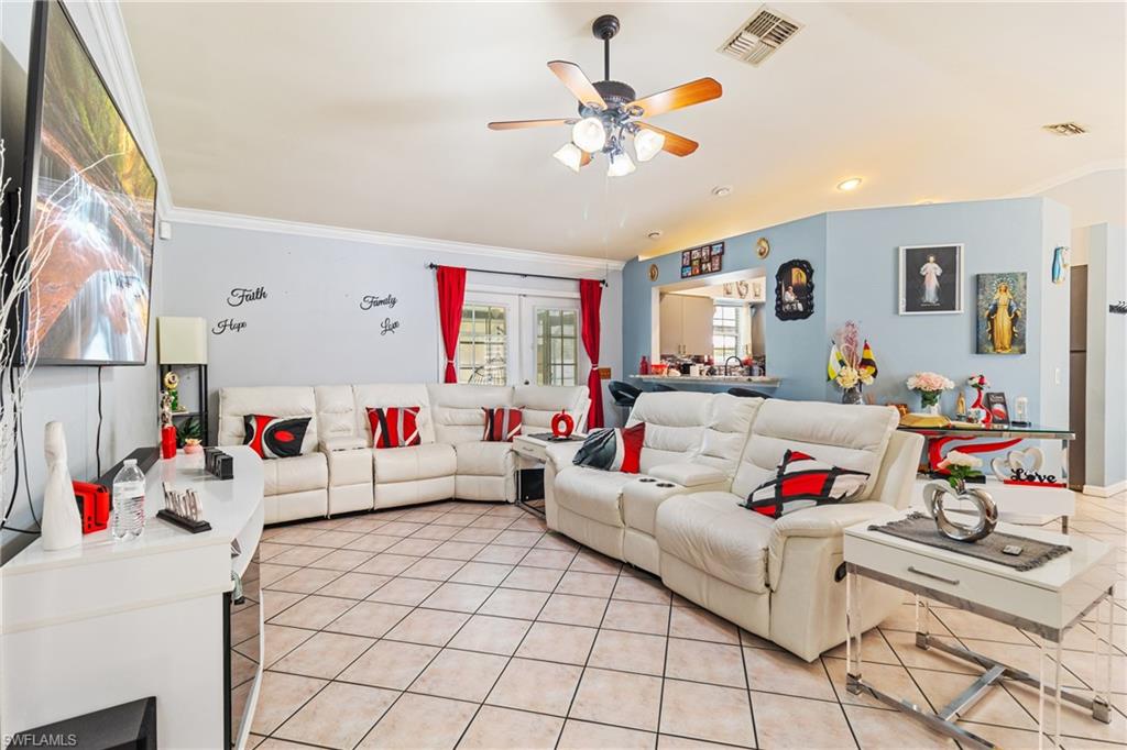 Living room with crown molding, light tile patterned floors, a ceiling fan, and suspended lighting