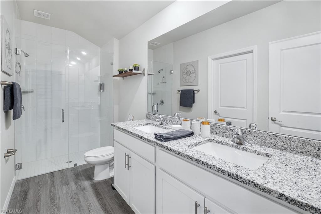 Bathroom featuring a stall shower, double vanity, and dark wood-style flooring