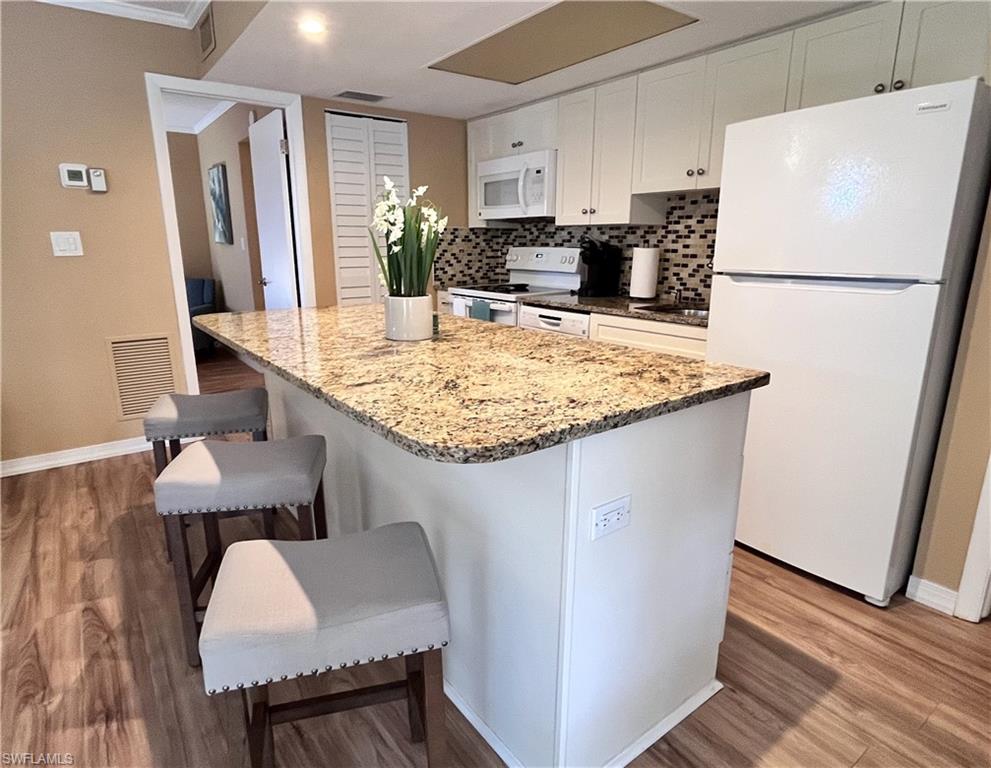 Beautifully updated kitchen featuring an oversized granite island with abundant storage, custom white cabinetry, and stylish wood-look plank flooring.