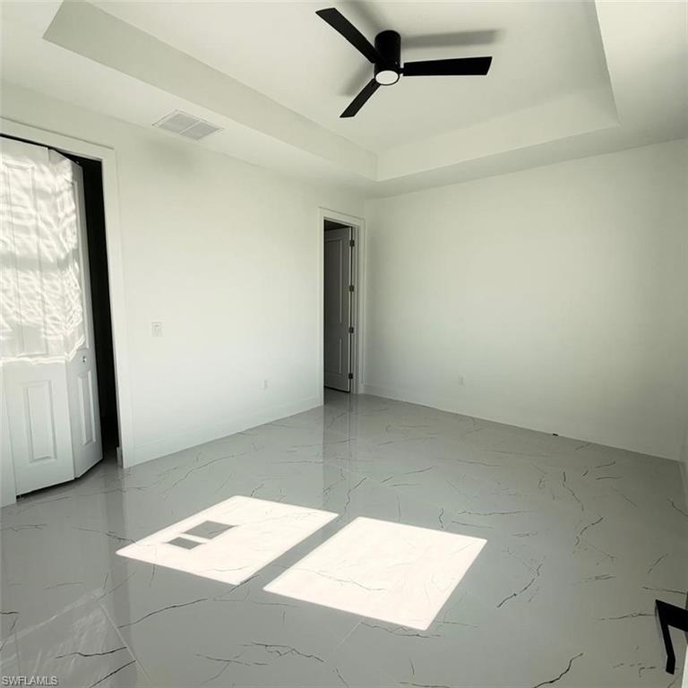 Empty room with a raised ceiling, ceiling fan, and light marble finish flooring