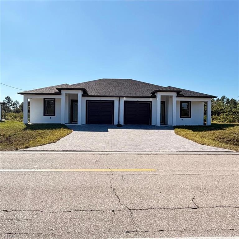 Prairie-style home with decorative driveway, an attached garage, roof with shingles, and a front yard