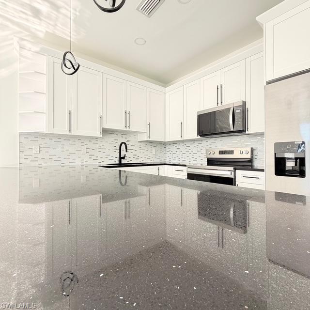 Kitchen with decorative light fixtures, white cabinets, stainless steel appliances, and dark stone countertops