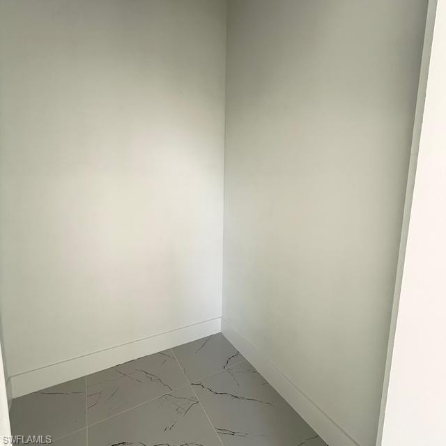 Unfurnished room with marble look tiles and baseboards