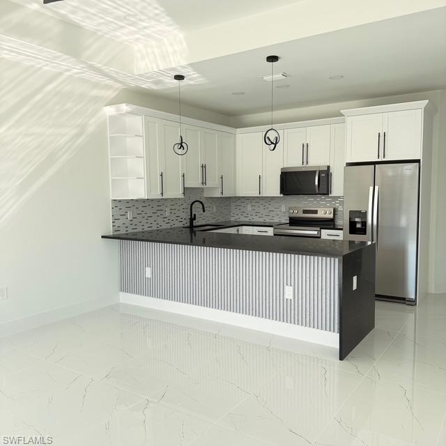Kitchen featuring backsplash, stainless steel appliances, white cabinetry, and a peninsula