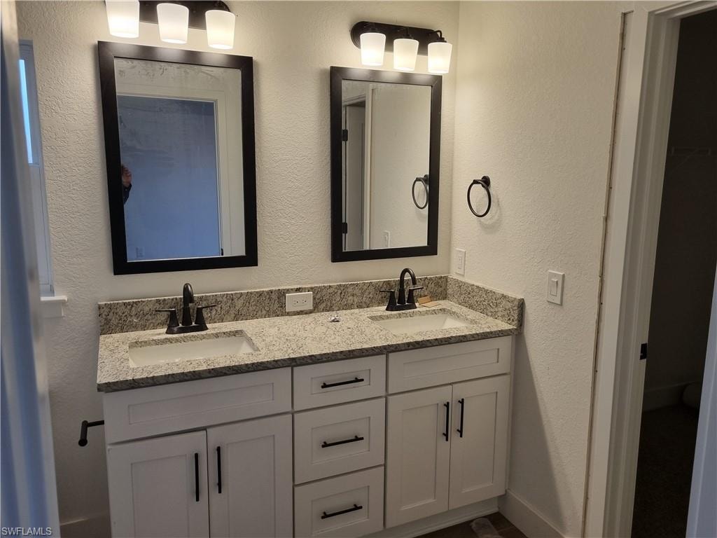 Full bathroom featuring a textured wall and double vanity