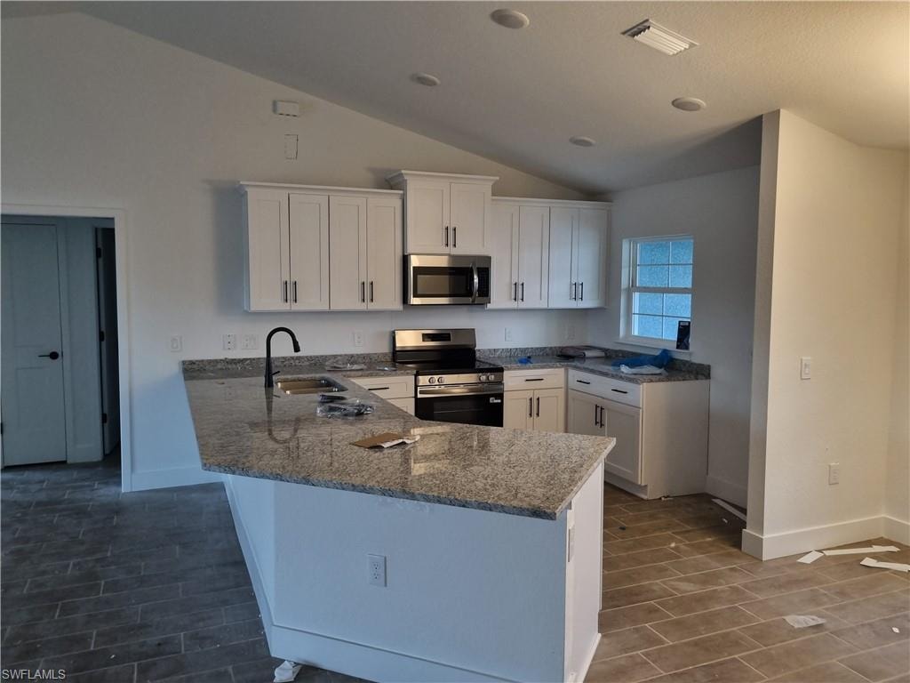 Kitchen with white cabinets, dark stone counters, stainless steel appliances, a peninsula, and wood finish floors