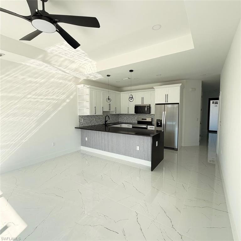 Kitchen with stainless steel appliances, light marble finish floors, backsplash, hanging light fixtures, and white cabinetry