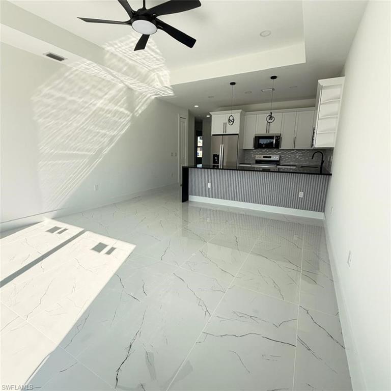 Unfurnished living room featuring a ceiling fan, a raised ceiling, light marble finish floors, and recessed lighting