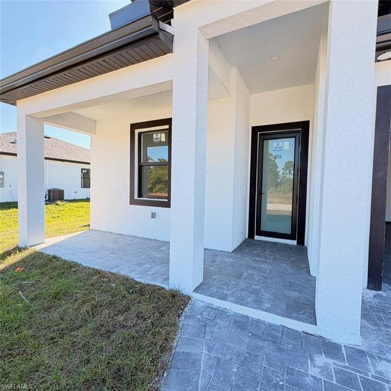 View of exterior entry with a patio area, a lawn, and stucco siding