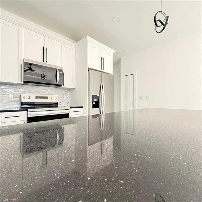 Kitchen featuring stainless steel appliances, white cabinetry, backsplash, and dark stone counters