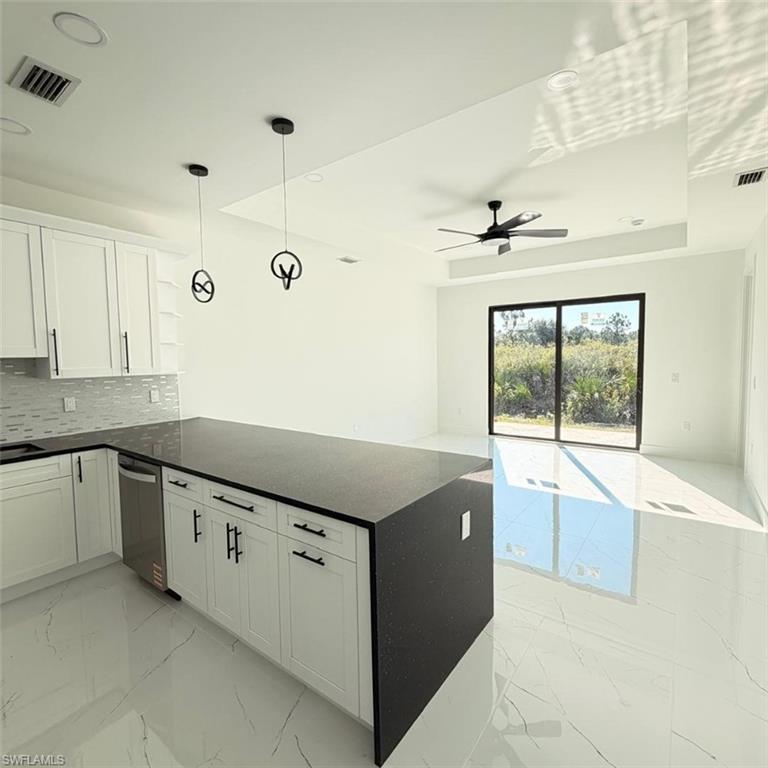 Kitchen with decorative light fixtures, light marble finish flooring, white cabinetry, open floor plan, and dark stone countertops