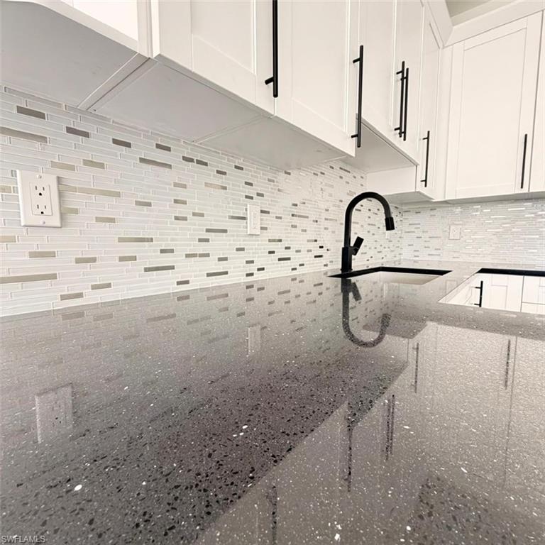 Kitchen view of dark stone counters, white cabinets, and tasteful backsplash
