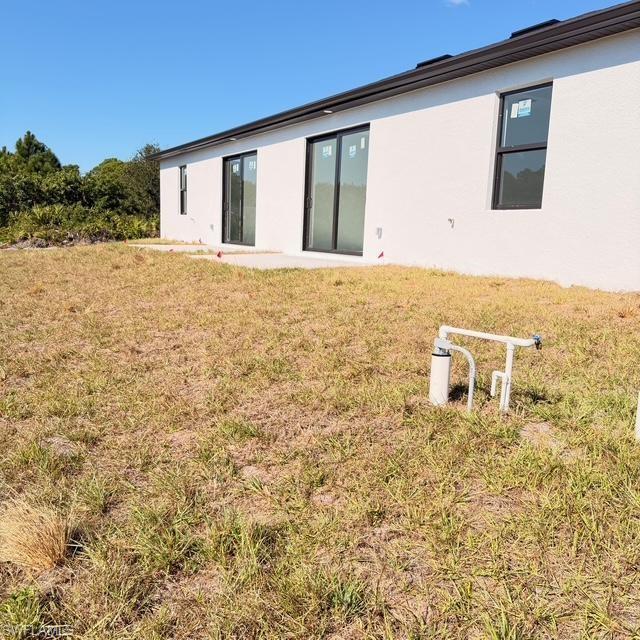 Back of house featuring a lawn, stucco siding, and a patio