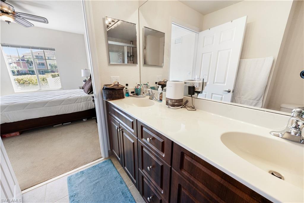 Ensuite bathroom featuring light carpet, double vanity, light tile patterned floors, a ceiling fan, and a shower with door