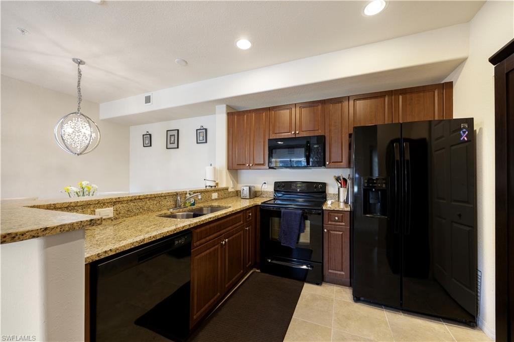 Kitchen featuring black appliances, light stone counters, a peninsula, light tile patterned floors, and wood finish cabinets