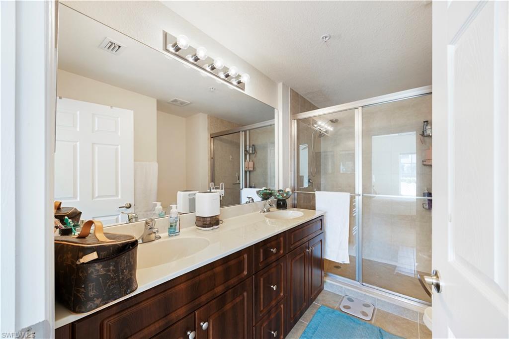 Full bath with double vanity, a stall shower, and light tile patterned flooring