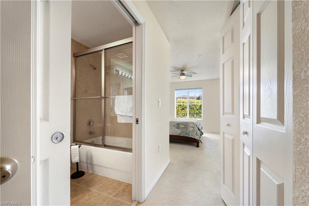 Ensuite bathroom featuring combined bath / shower with glass door, light carpet, a textured ceiling, light tile patterned floors, and a ceiling fan