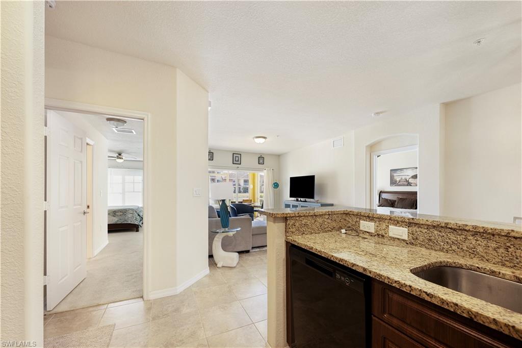 Kitchen with black dishwasher, light stone counters, light colored carpet, dark wood finish cabinets, and open floor plan