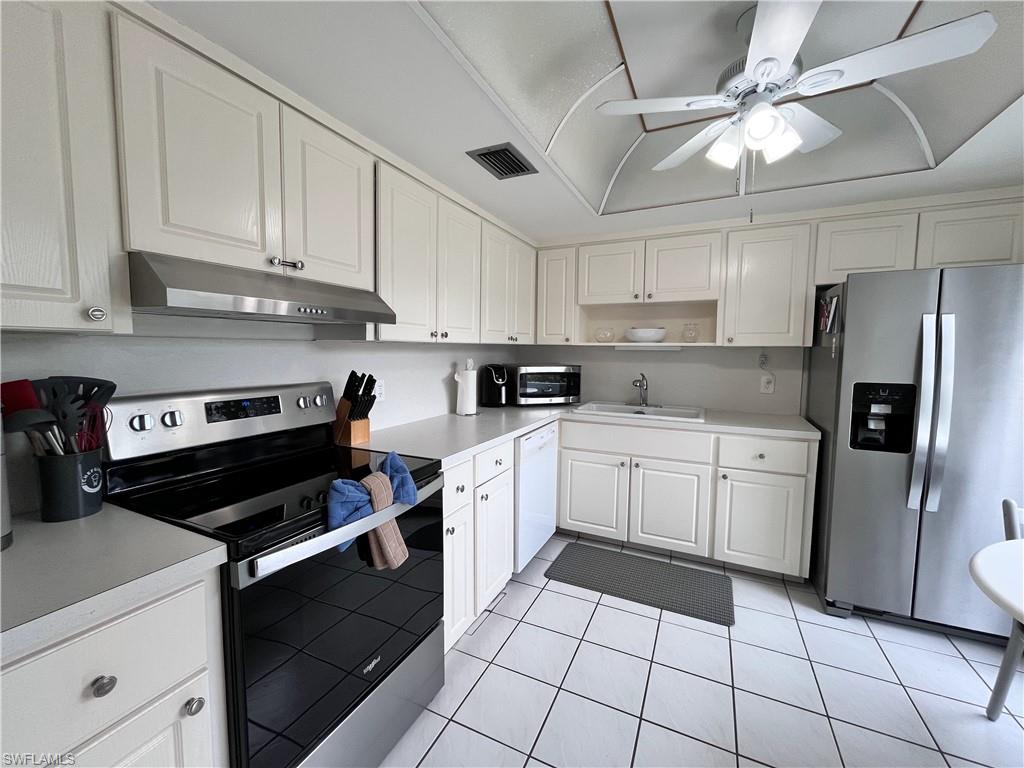 Kitchen with stainless steel appliances, light countertops, white cabinets, tile flooring and small table to enjoy a meal looking out the large window to the courtyard.