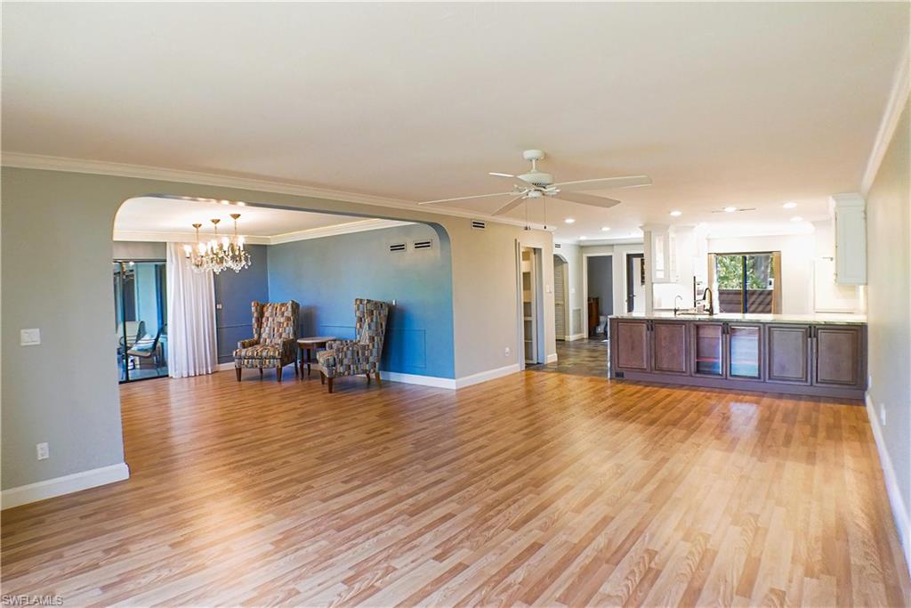 Spare room featuring arched walkways, ceiling fan, light wood-type flooring, suspended lighting, and crown molding