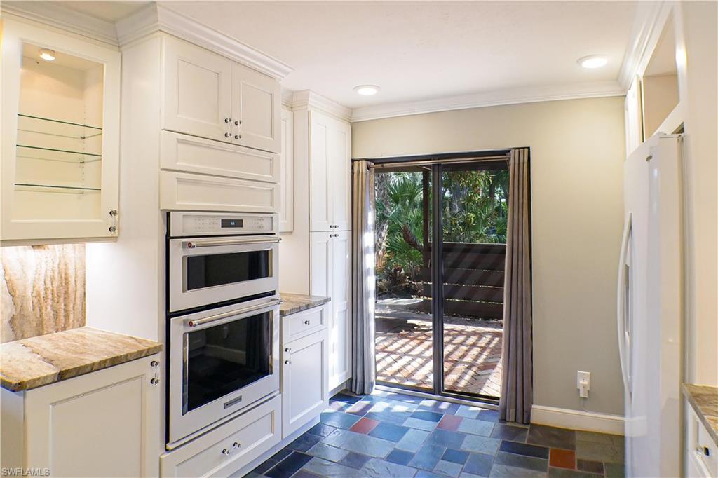 Kitchen with glass fronted cabinets, white cabinets, freestanding refrigerator, dark stone finish floors, and black electric cooktop