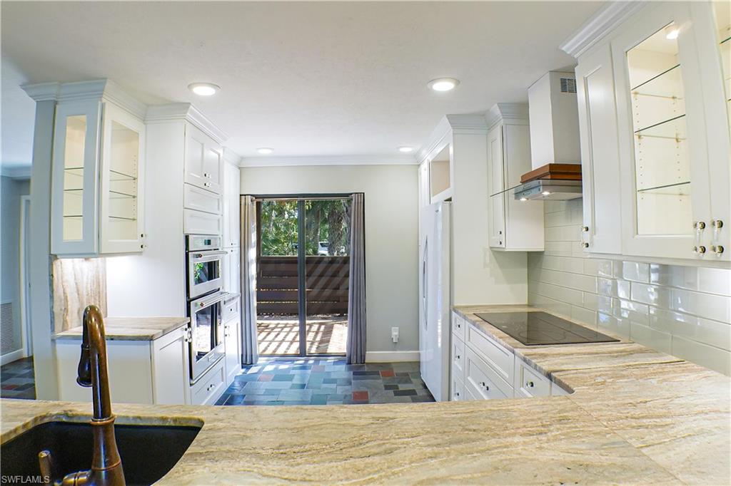 Kitchen featuring white refrigerator with ice dispenser, white cabinetry, light stone counters, glass insert cabinets, and ornamental molding
