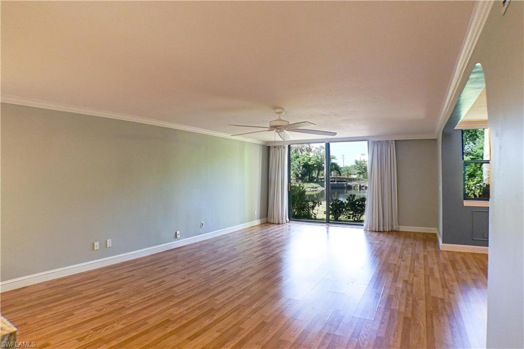 Unfurnished living room with arched walkways, light wood finished floors, ornamental molding, ceiling fan, and a chandelier