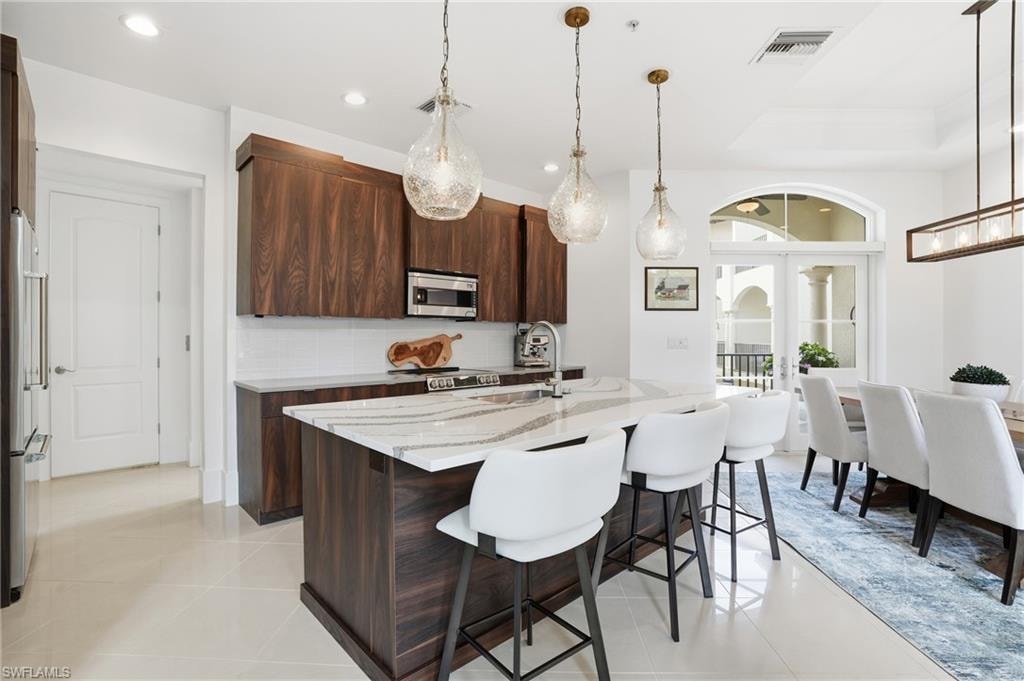 Kitchen with light stone countertops, a kitchen breakfast bar, modern cabinets, a kitchen island with sink, and light tile patterned floors