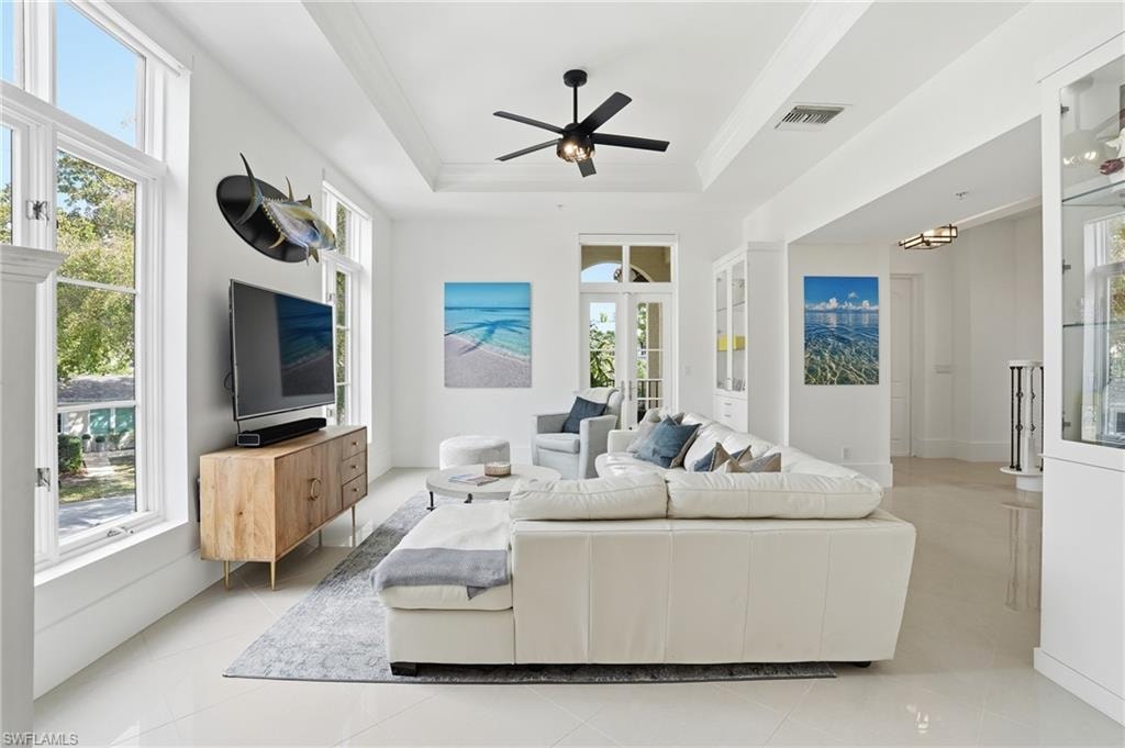 Living room featuring light tile patterned flooring, a ceiling fan, and a raised ceiling