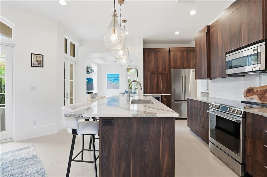 Kitchen featuring stainless steel appliances, modern cabinets, a kitchen breakfast bar, backsplash, and a center island with sink