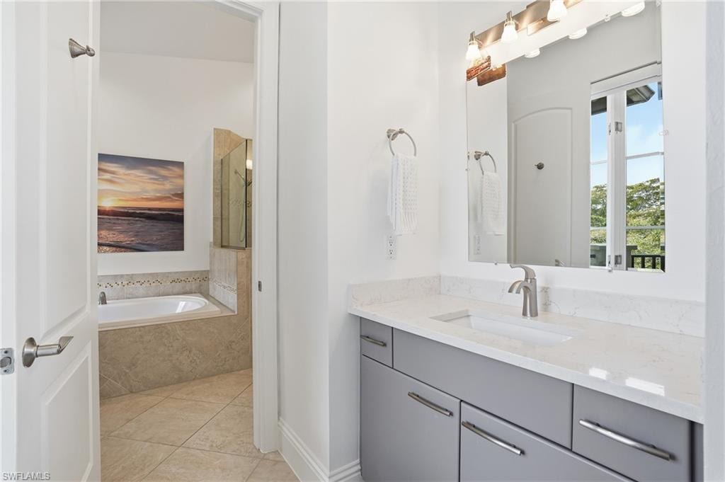 Full bathroom featuring vanity, a garden tub, and light tile patterned floors
