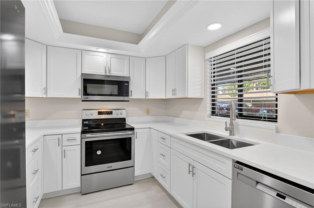 Kitchen featuring stainless steel appliances, white cabinets, light stone counters, recessed lighting, and a tray ceiling