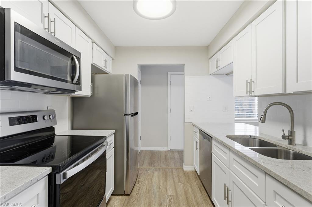 Kitchen featuring stainless steel appliances, tasteful backsplash, light stone countertops, white cabinets, and light wood-style flooring