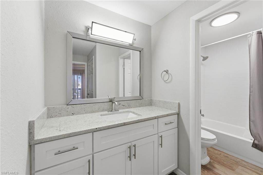 Bathroom featuring shower / bathtub combination with curtain, vanity, light wood-style floors, and a textured wall