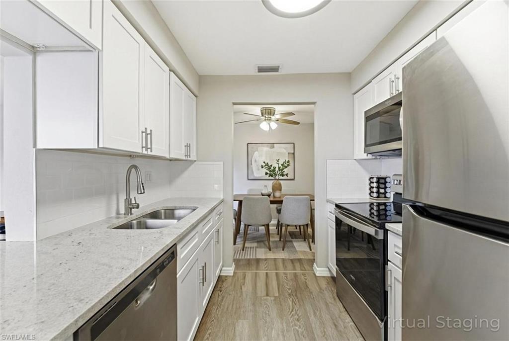 Kitchen featuring stainless steel appliances, backsplash, light stone countertops, and white cabinets
