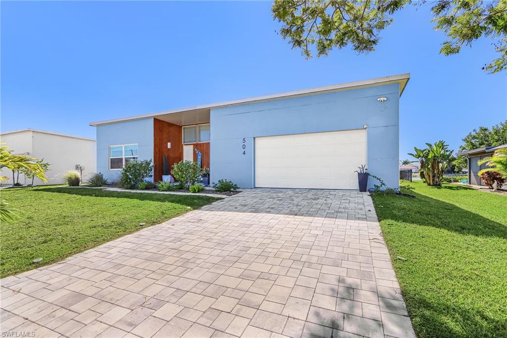 Contemporary house featuring a front yard, decorative driveway, stucco siding, and an attached garage